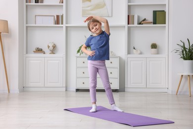 Photo of Cute little girl exercising on fitness mat indoors