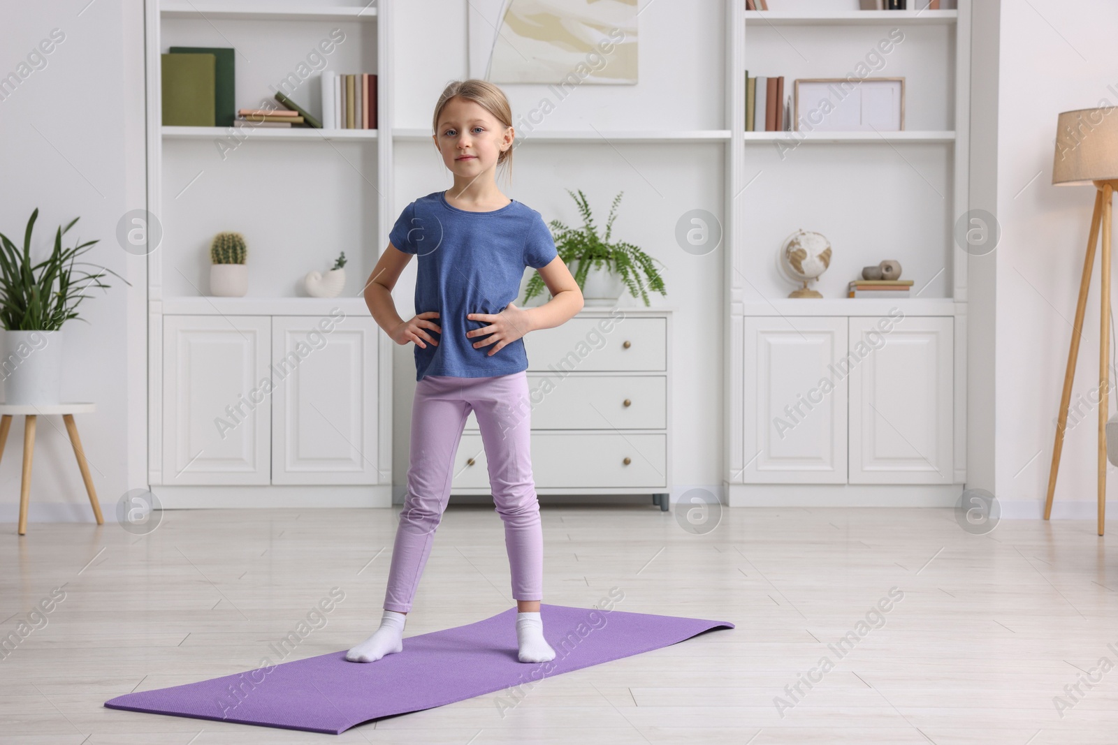 Photo of Cute little girl exercising on fitness mat indoors