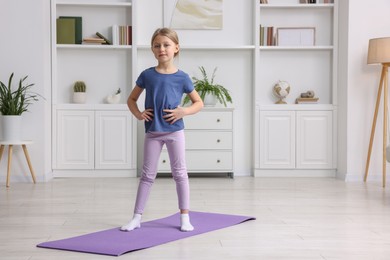 Photo of Cute little girl exercising on fitness mat indoors