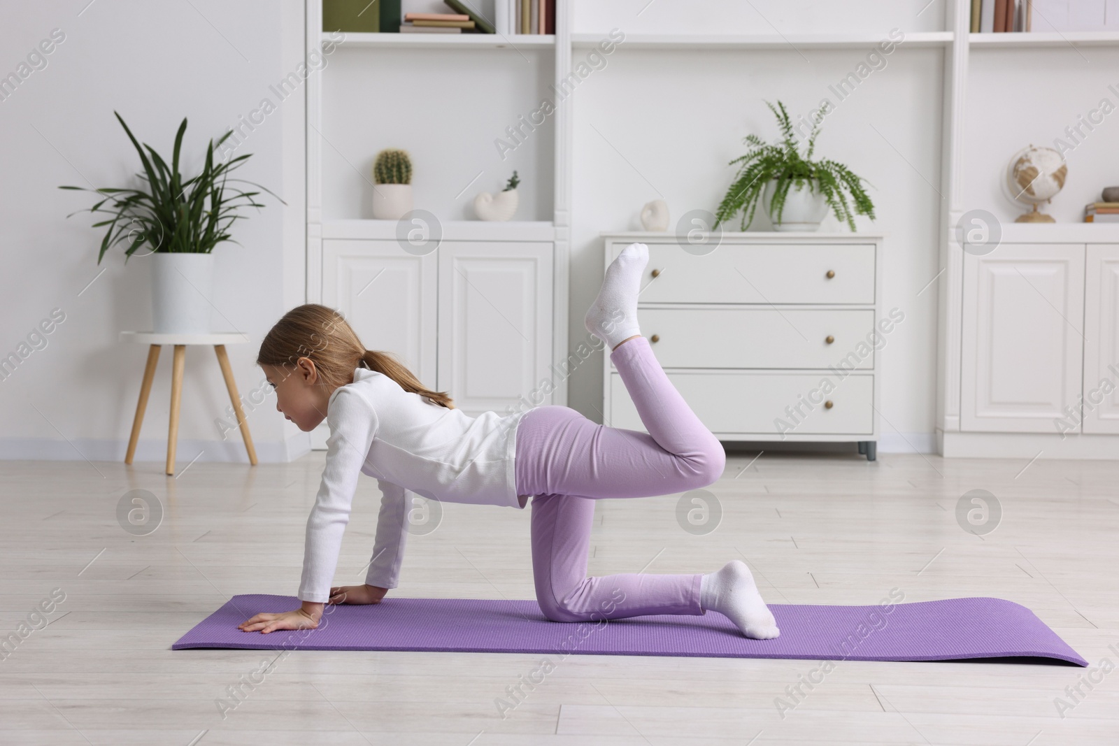 Photo of Cute little girl exercising on fitness mat indoors