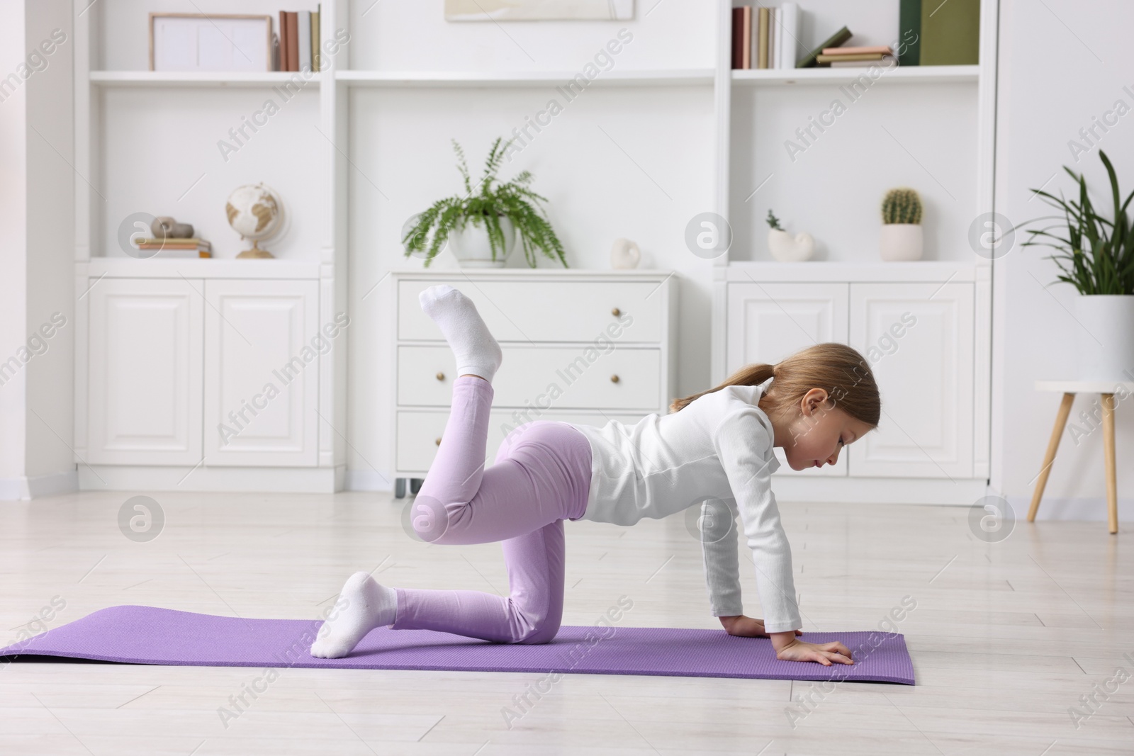 Photo of Cute little girl exercising on fitness mat indoors