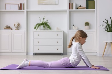 Photo of Cute little girl exercising on fitness mat indoors