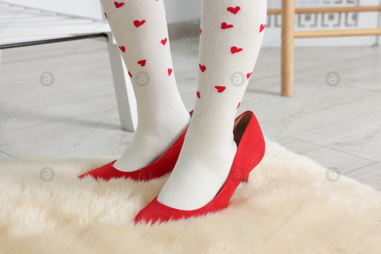 Photo of Little girl wearing oversized high heeled shoes indoors, closeup