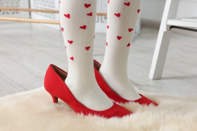 Photo of Little girl wearing oversized high heeled shoes indoors, closeup