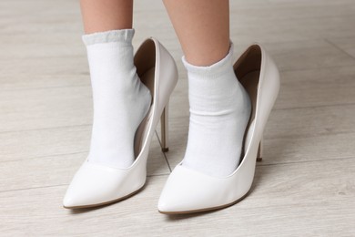 Photo of Little girl wearing oversized high heeled shoes indoors, closeup