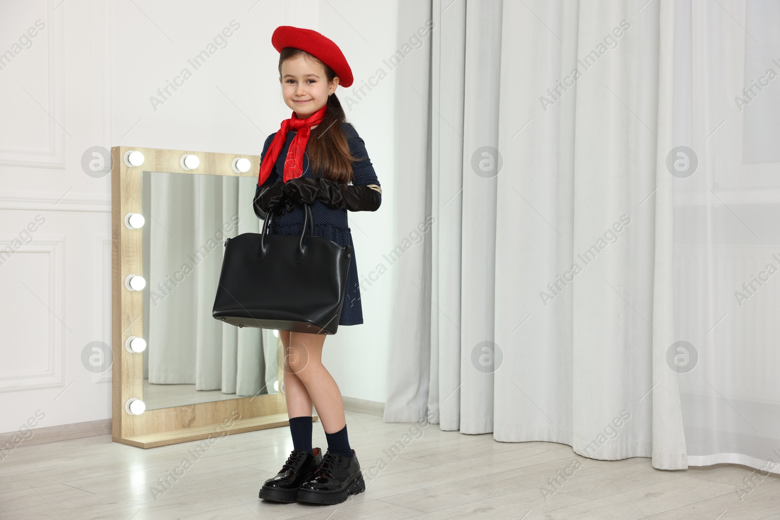 Photo of Stylish little girl wearing oversized shoes indoors, space for text