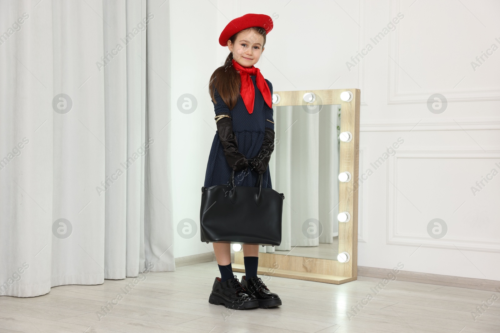 Photo of Stylish little girl wearing oversized shoes indoors