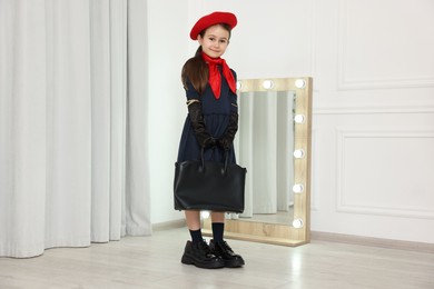 Photo of Stylish little girl wearing oversized shoes indoors