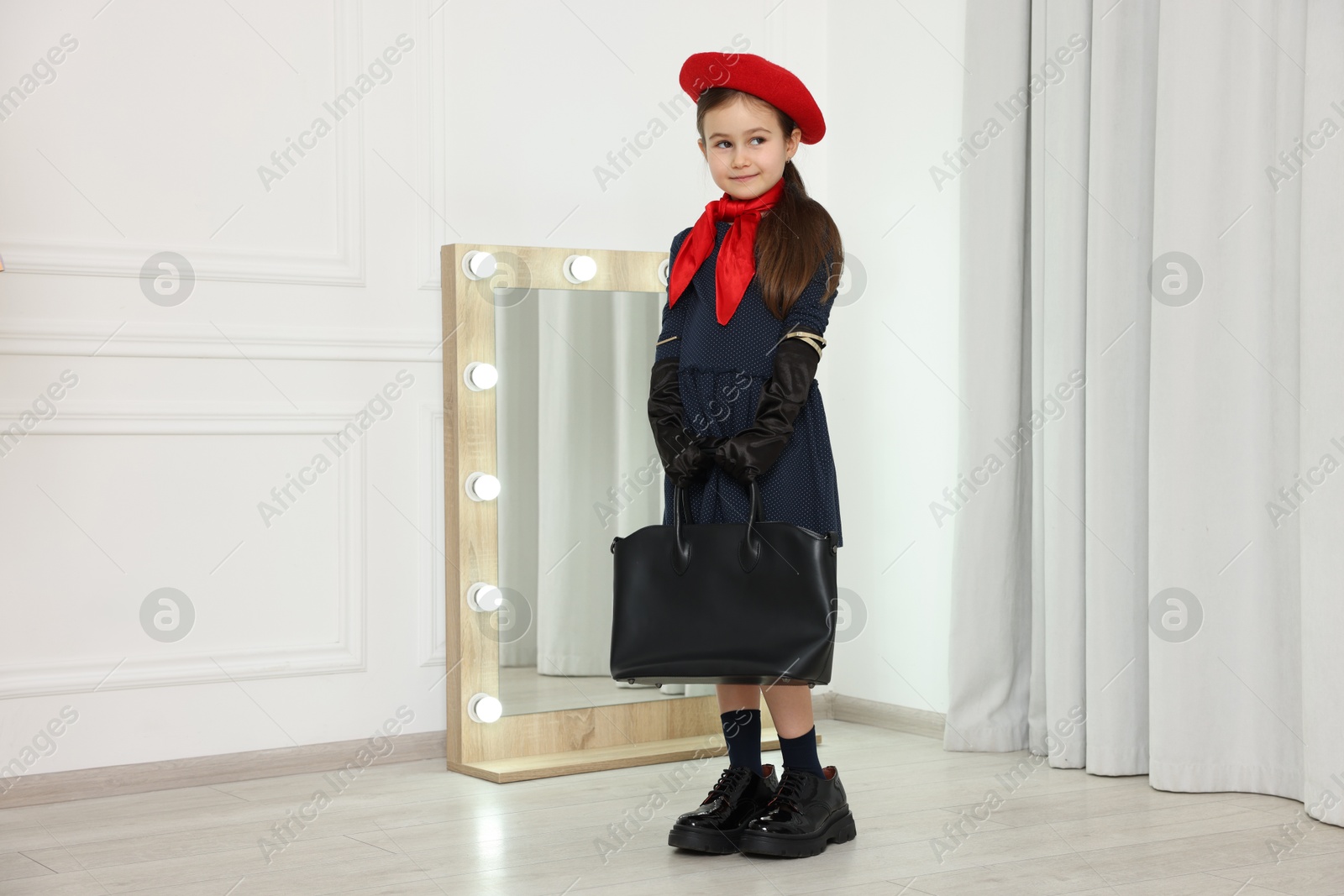 Photo of Stylish little girl wearing oversized shoes indoors