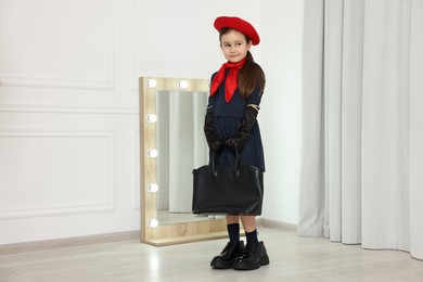 Photo of Stylish little girl wearing oversized shoes indoors