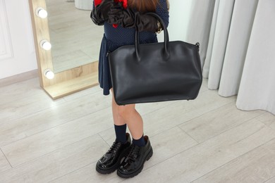 Photo of Stylish little girl wearing oversized shoes indoors, closeup