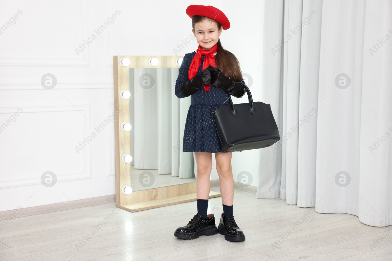 Photo of Stylish little girl wearing oversized shoes indoors