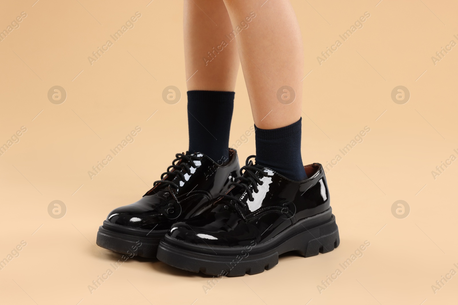 Photo of Child wearing oversized shoes on beige background, closeup