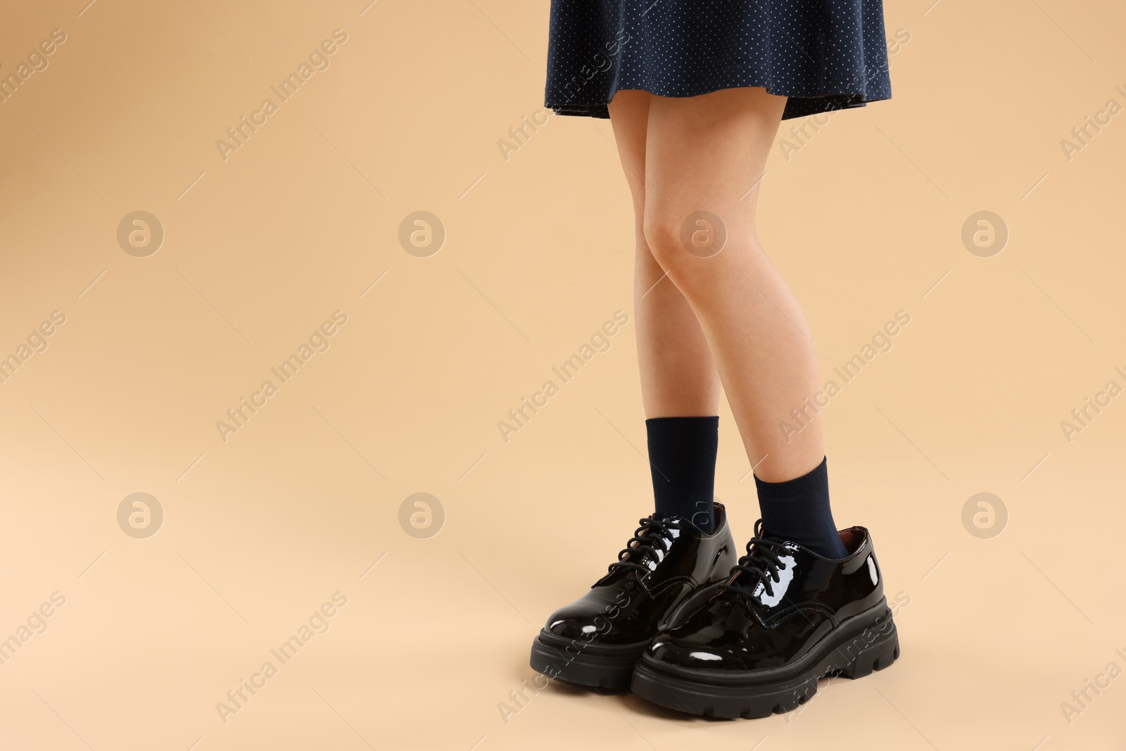 Photo of Child wearing oversized shoes on beige background, closeup. Space for text