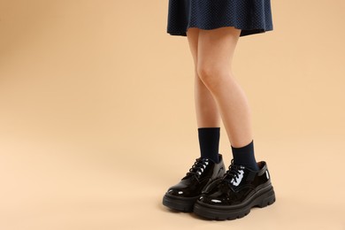 Photo of Child wearing oversized shoes on beige background, closeup. Space for text