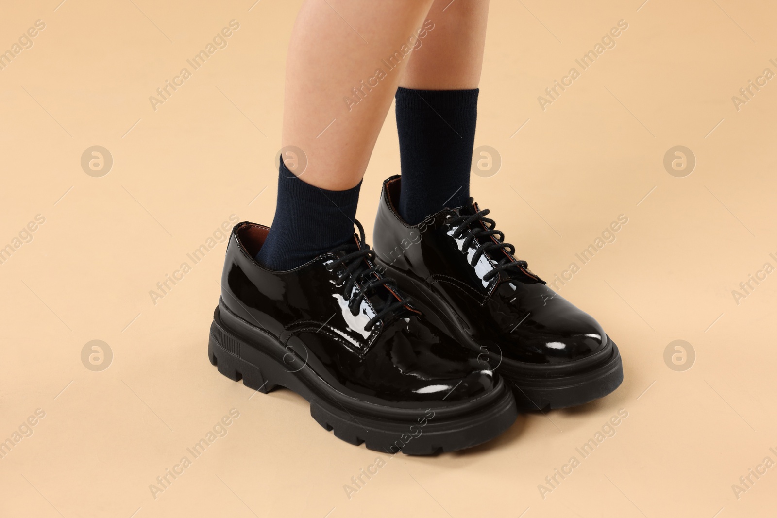 Photo of Child wearing oversized shoes on beige background, closeup