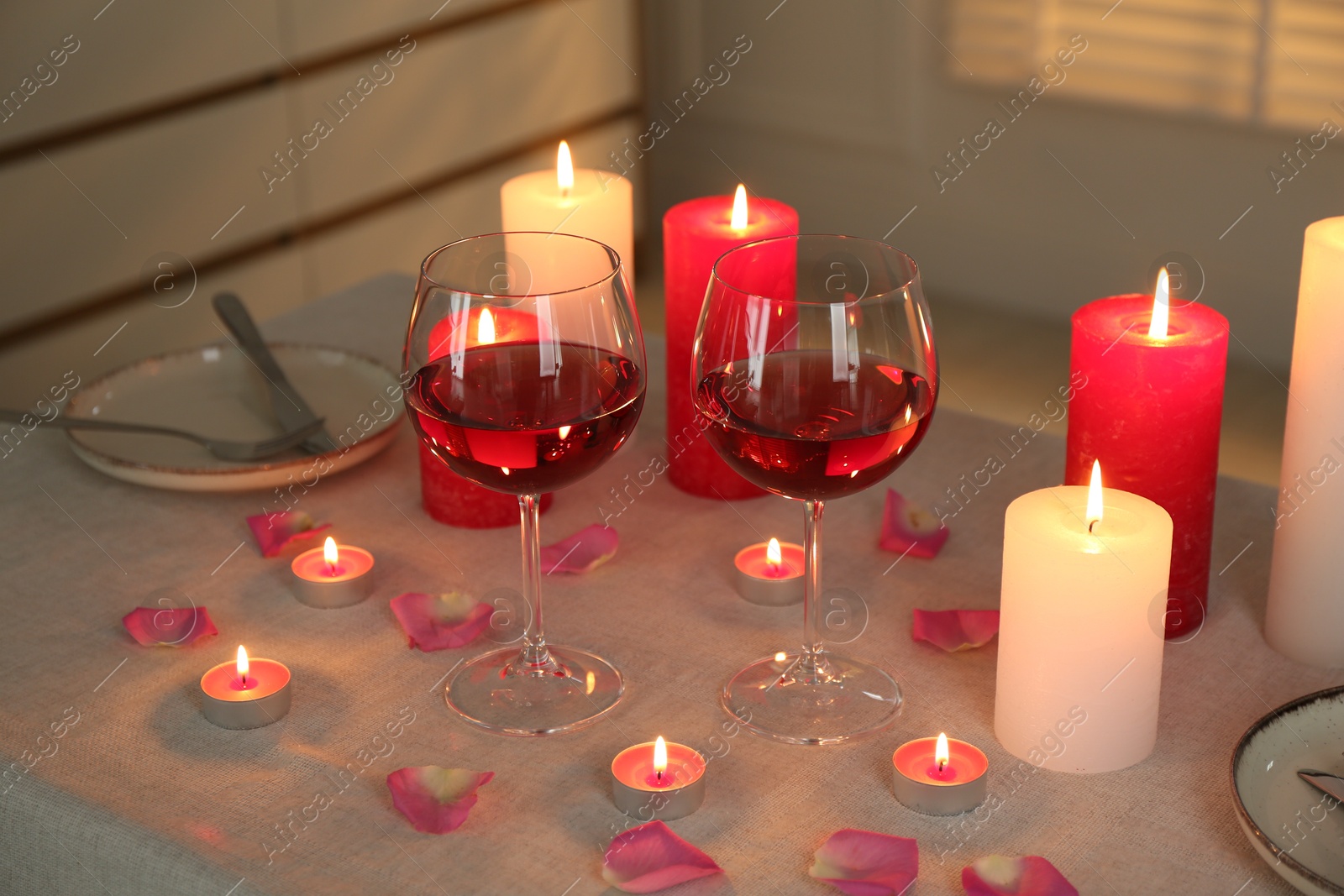 Photo of Romantic place setting with red wine, burning candles and petals on table