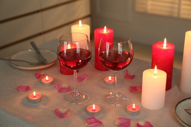 Photo of Romantic place setting with red wine, burning candles and petals on table