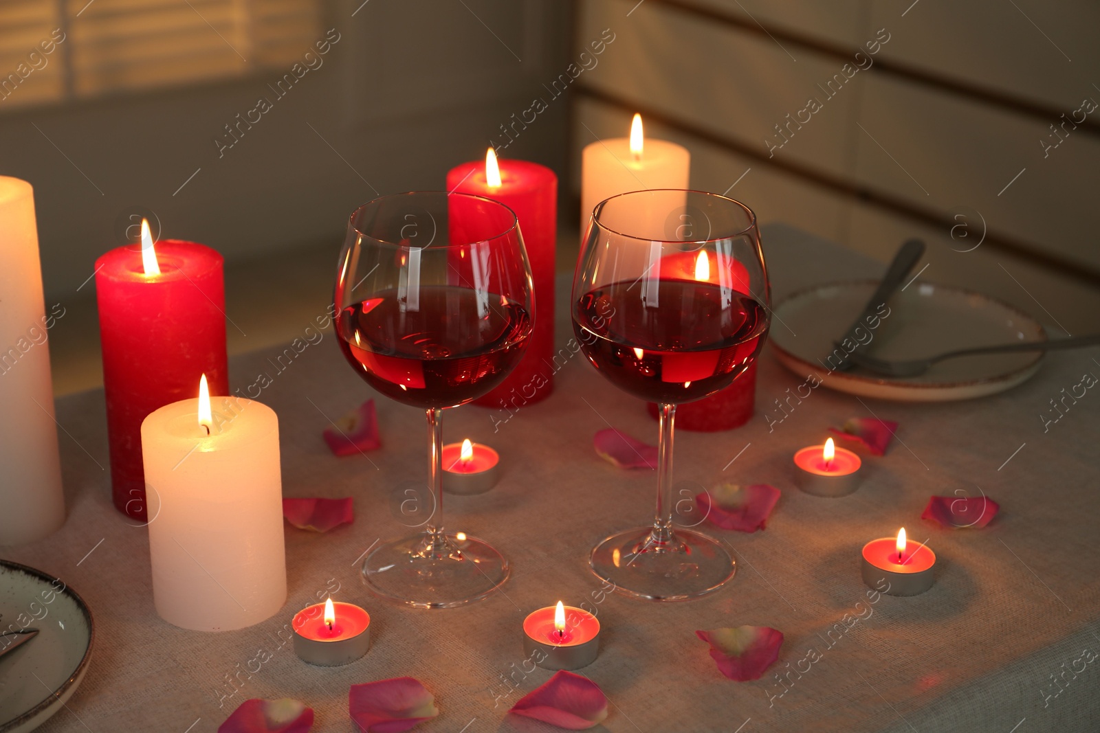 Photo of Romantic place setting with red wine, burning candles and petals on table