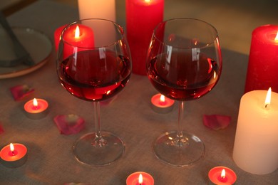 Photo of Romantic place setting with red wine, burning candles and petals on table, closeup