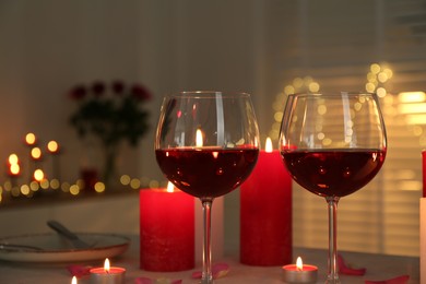 Photo of Romantic place setting with red wine and burning candles on table against blurred lights