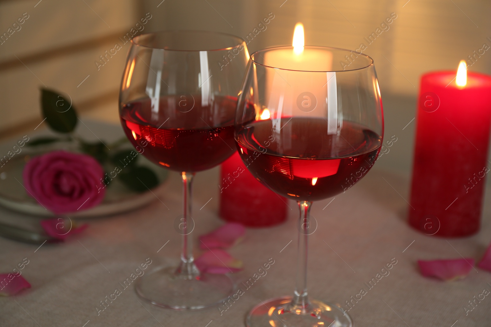 Photo of Romantic place setting with red wine, burning candles and rose on table, closeup.