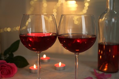 Romantic place setting with red wine, burning candles and rose on table against blurred lights, closeup