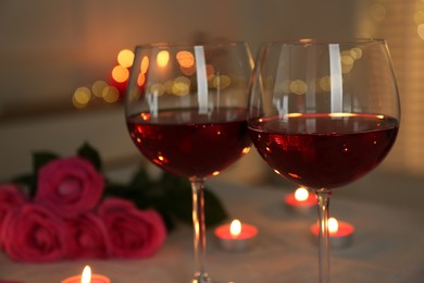 Romantic place setting with red wine, burning candles and roses on table against blurred lights, closeup