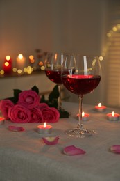 Photo of Romantic place setting with red wine, burning candles and roses on table against blurred lights