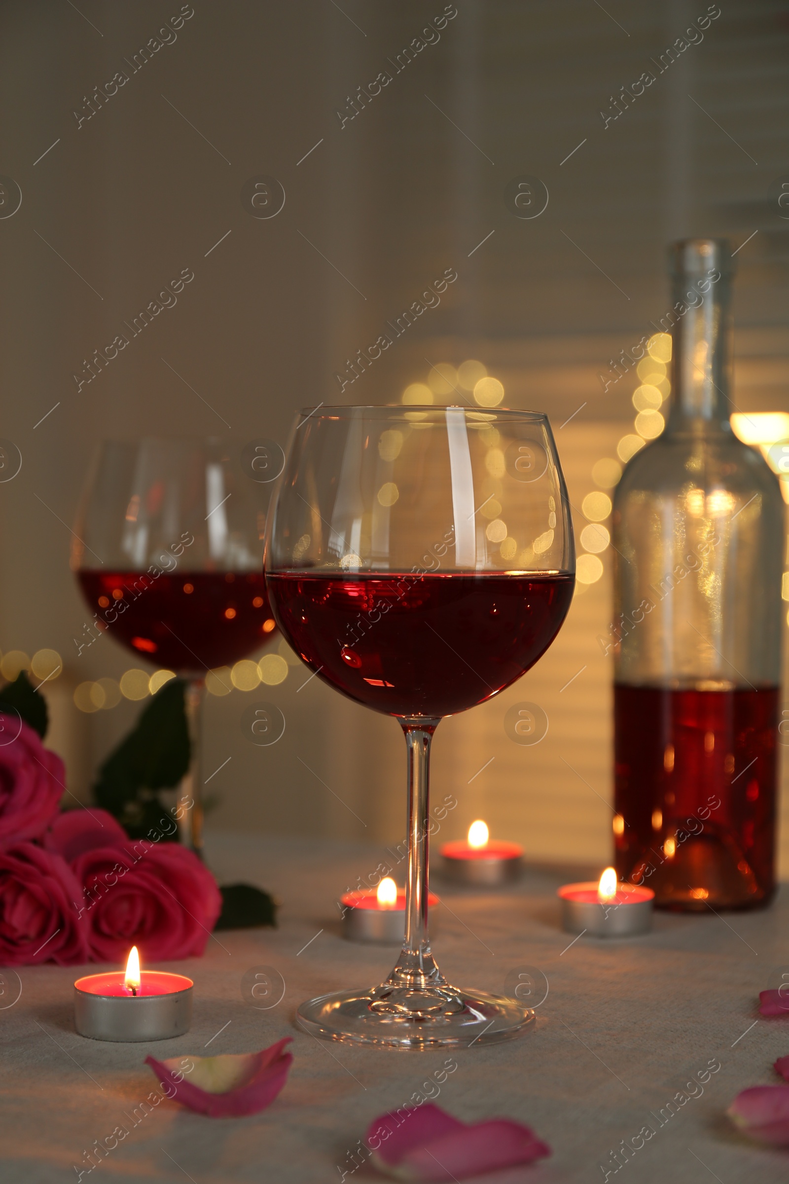 Photo of Romantic place setting with red wine and burning candles on table against blurred lights, closeup