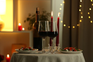 Photo of Romantic place setting with red wine and burning candles on table in restaurant