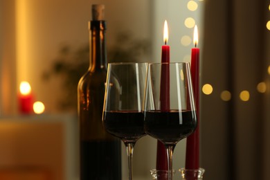 Glasses of red wine and burning candles against blurred lights, closeup. Romantic dinner