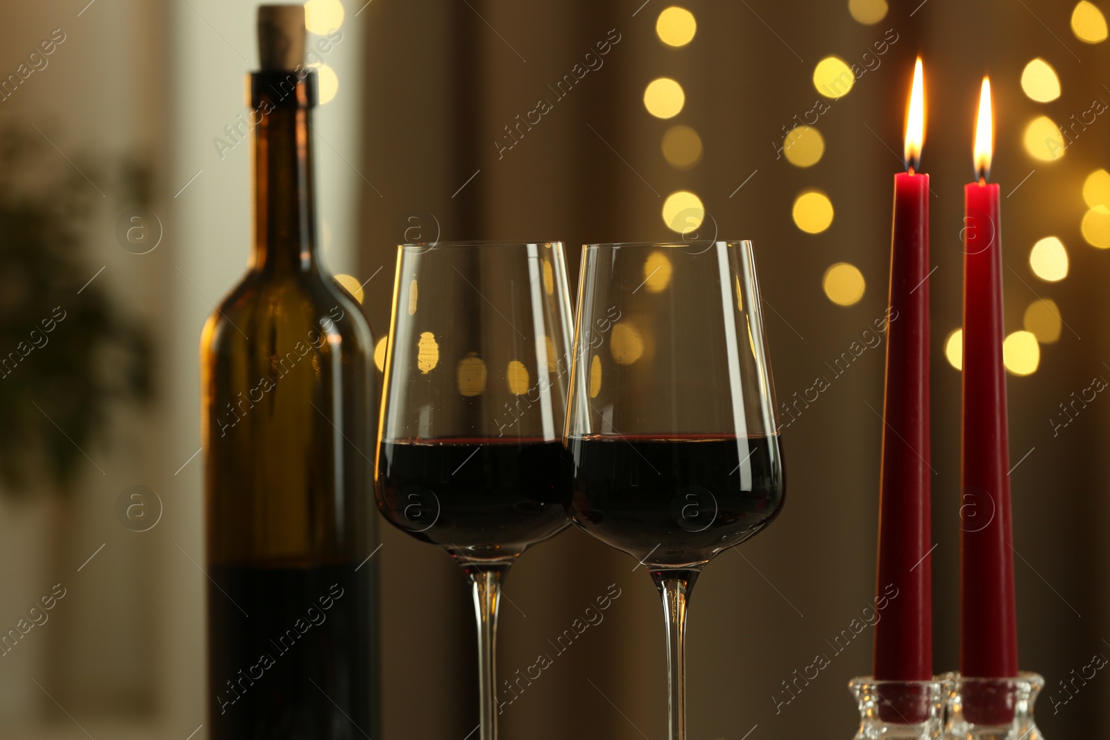 Photo of Glasses of red wine and burning candles against blurred lights, closeup. Romantic dinner