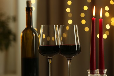 Glasses of red wine and burning candles against blurred lights, closeup. Romantic dinner