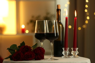 Photo of Glasses of red wine, burning candles and roses on table in restaurant. Romantic dinner