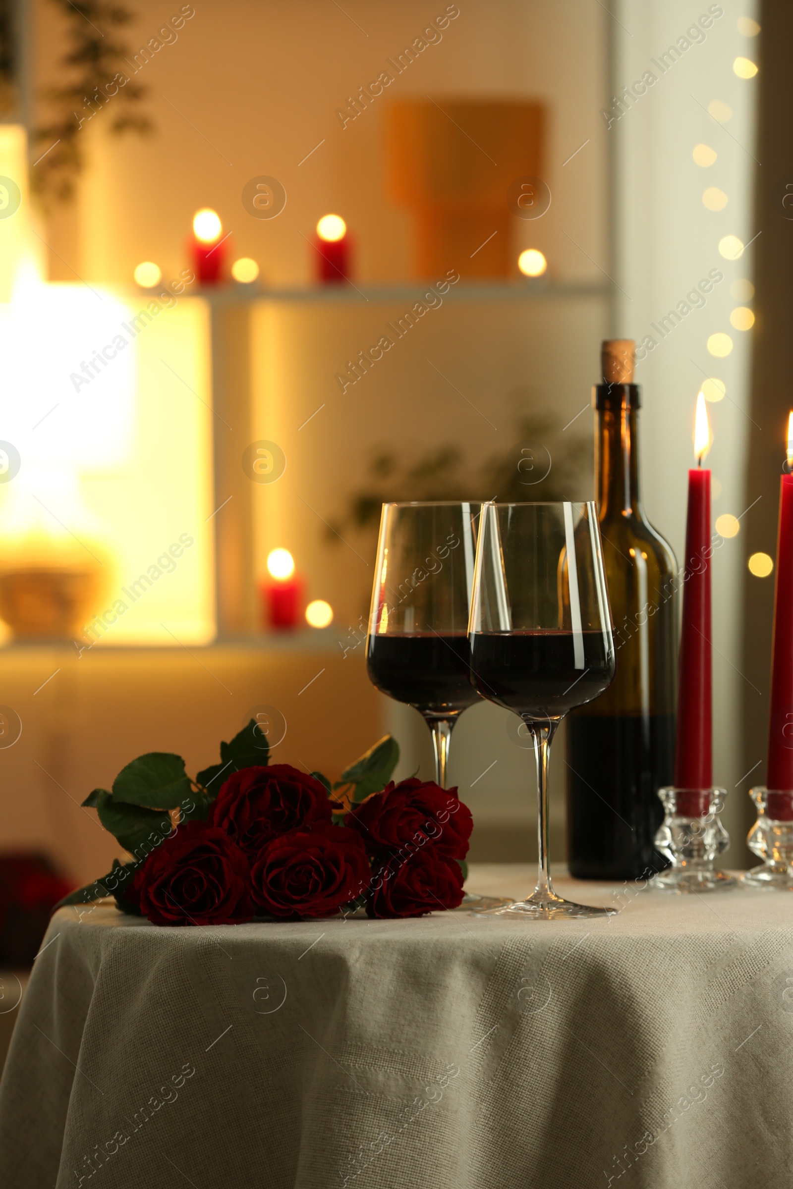 Photo of Glasses of red wine, burning candles and roses on table in restaurant. Romantic dinner