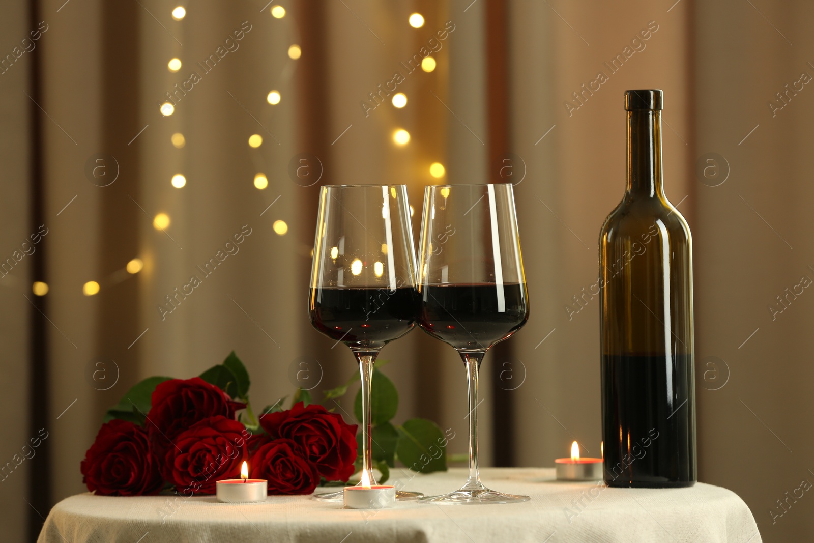 Photo of Glasses of red wine, burning candles and roses on table in restaurant. Romantic dinner