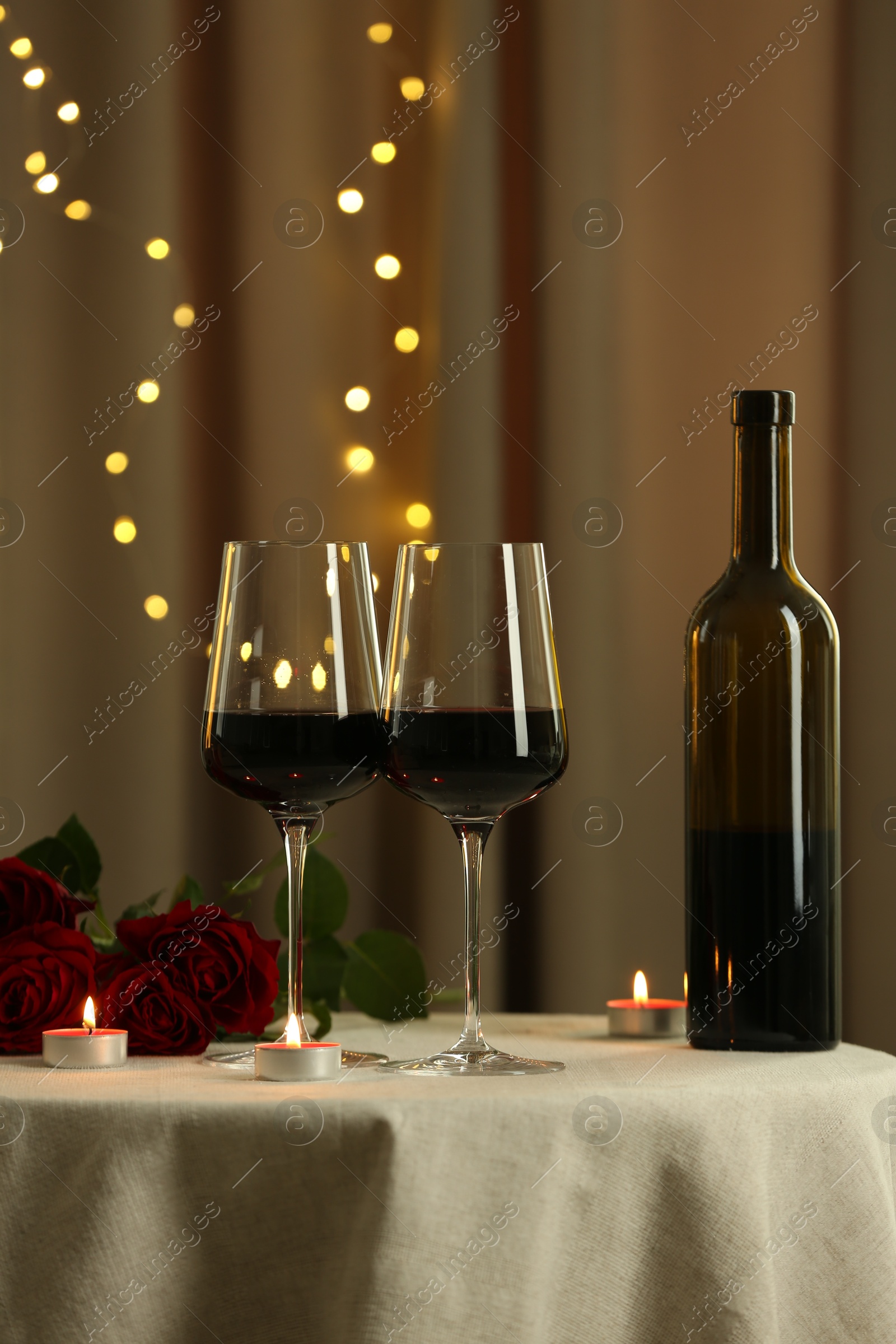 Photo of Glasses of red wine, burning candles and roses on table in restaurant. Romantic dinner