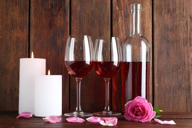 Glasses of red wine, bottle, burning candles and rose on wooden table