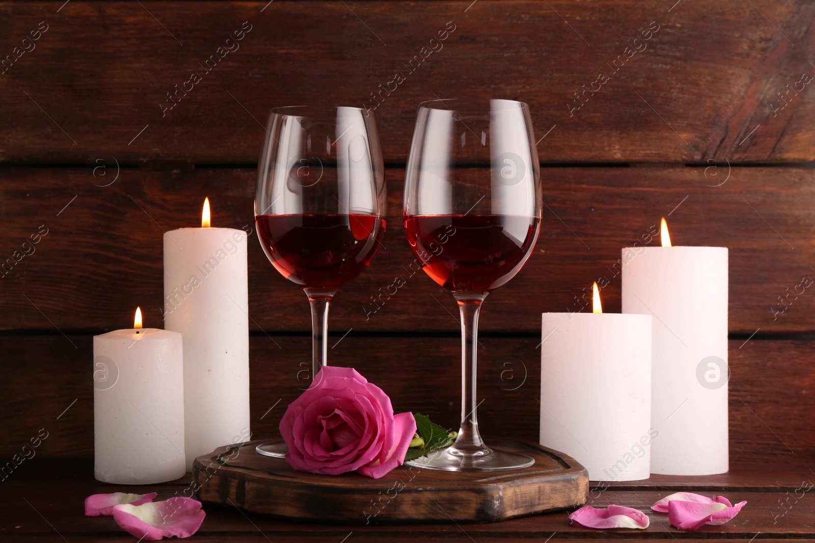 Photo of Glasses of red wine, burning candle and rose on wooden table