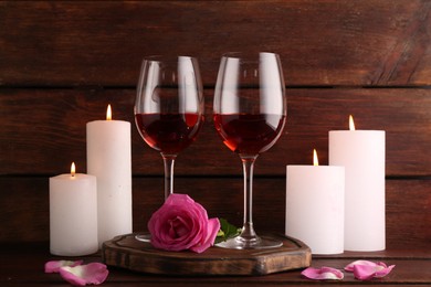 Glasses of red wine, burning candle and rose on wooden table