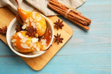 Photo of Delicious pears with caramel sauce, almond flakes and spices on blue wooden table, flat lay. Space for text