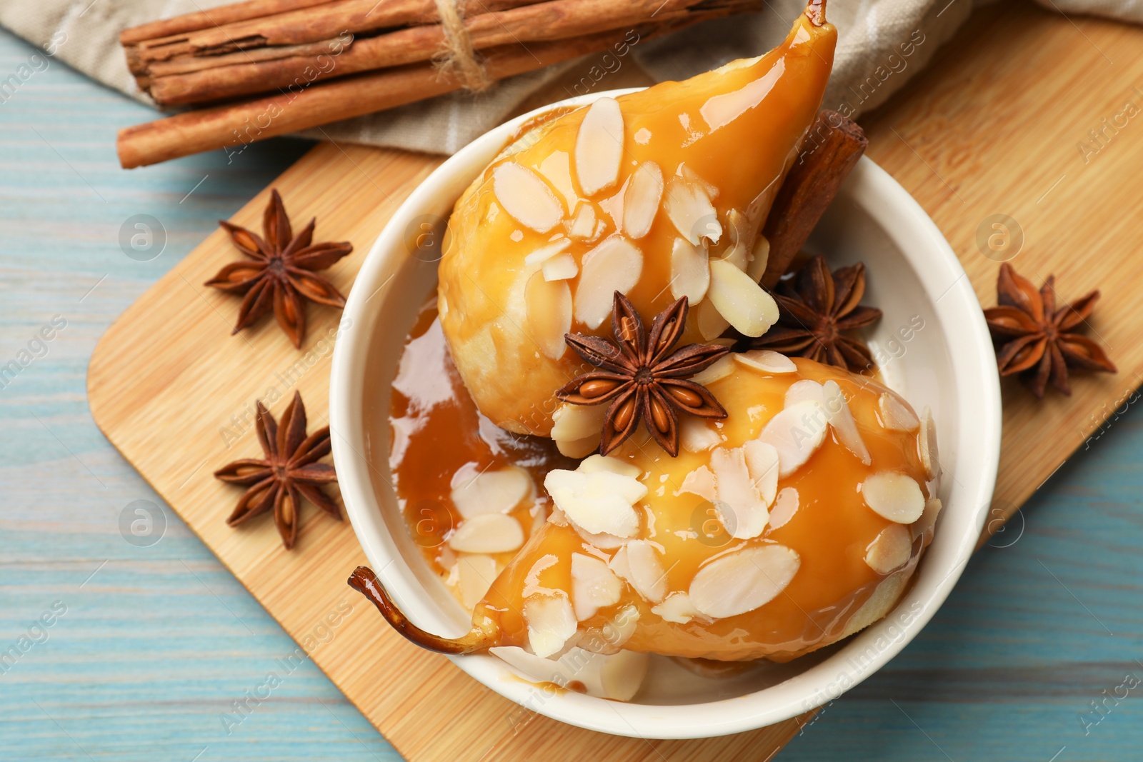 Photo of Delicious pears with caramel sauce, almond flakes and spices on blue wooden table, flat lay