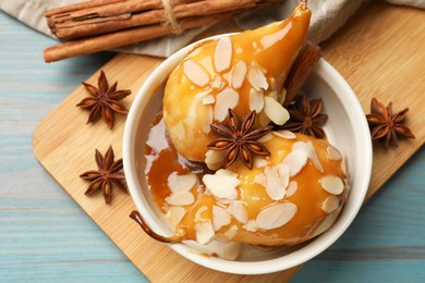 Delicious pears with caramel sauce, almond flakes and spices on blue wooden table, flat lay