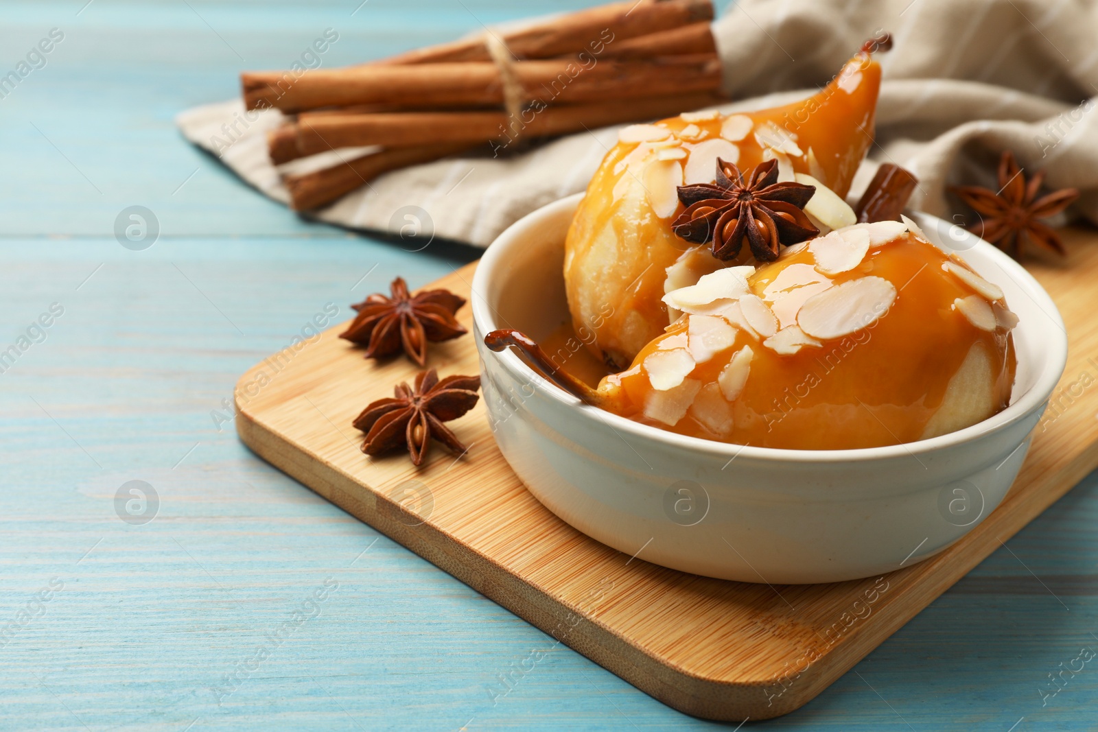 Photo of Delicious pears with caramel sauce, almond flakes and spices on blue wooden table, closeup