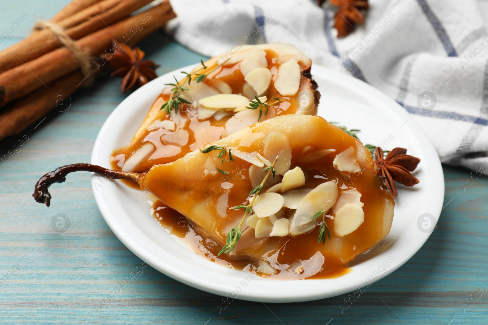 Photo of Delicious pears with caramel sauce, almond flakes and spices on blue wooden table, closeup