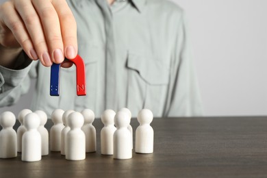 Photo of Woman with magnet attracting human figures at wooden table, closeup