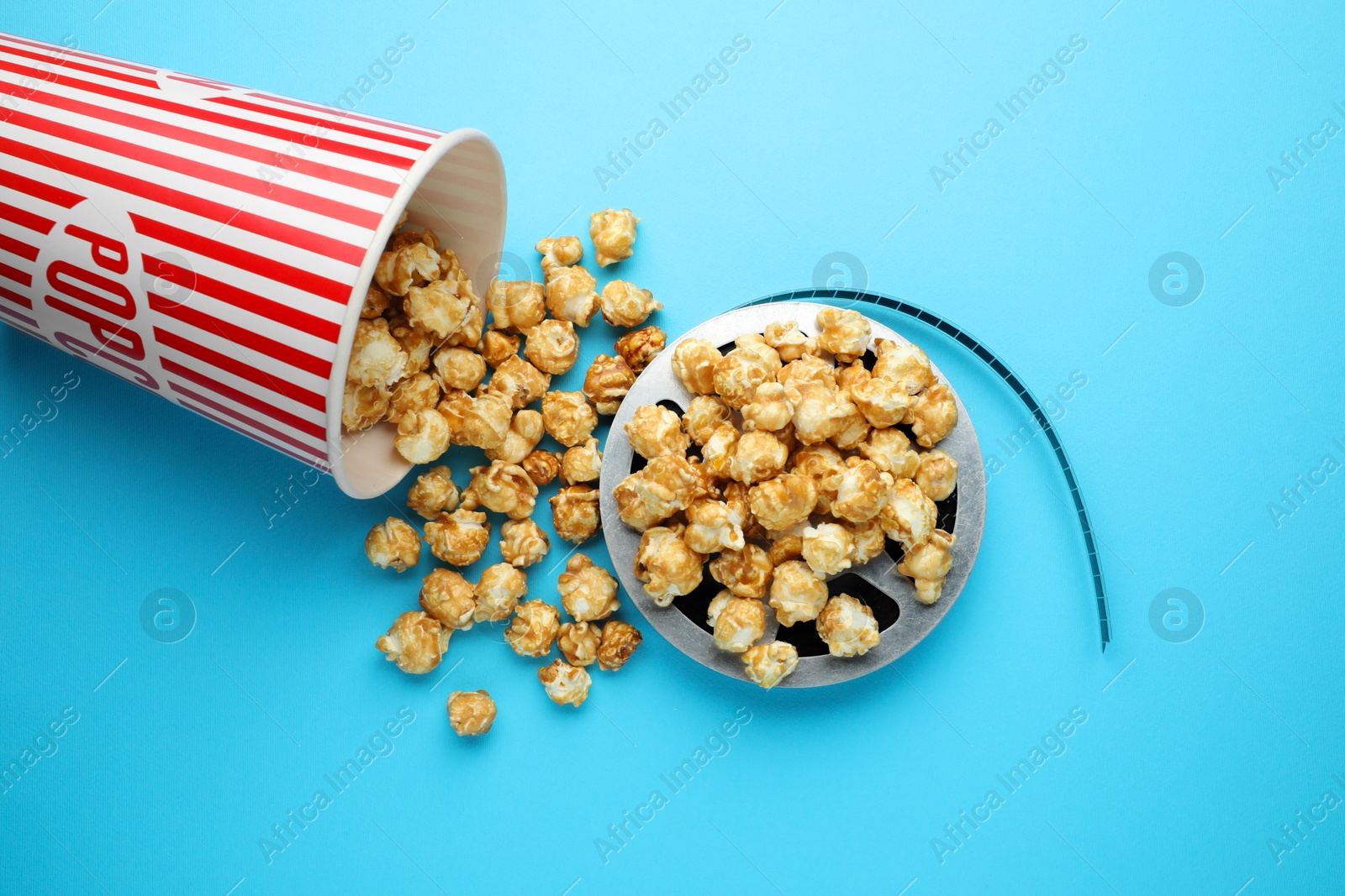 Photo of Sweet popcorn and film reel on light blue background, top view. Watching movie