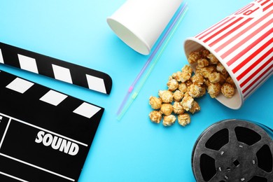 Photo of Movie clapper, sweet popcorn and film reel on light blue background, flat lay