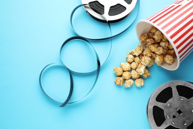 Photo of Sweet popcorn and film reels on light blue background, flat lay